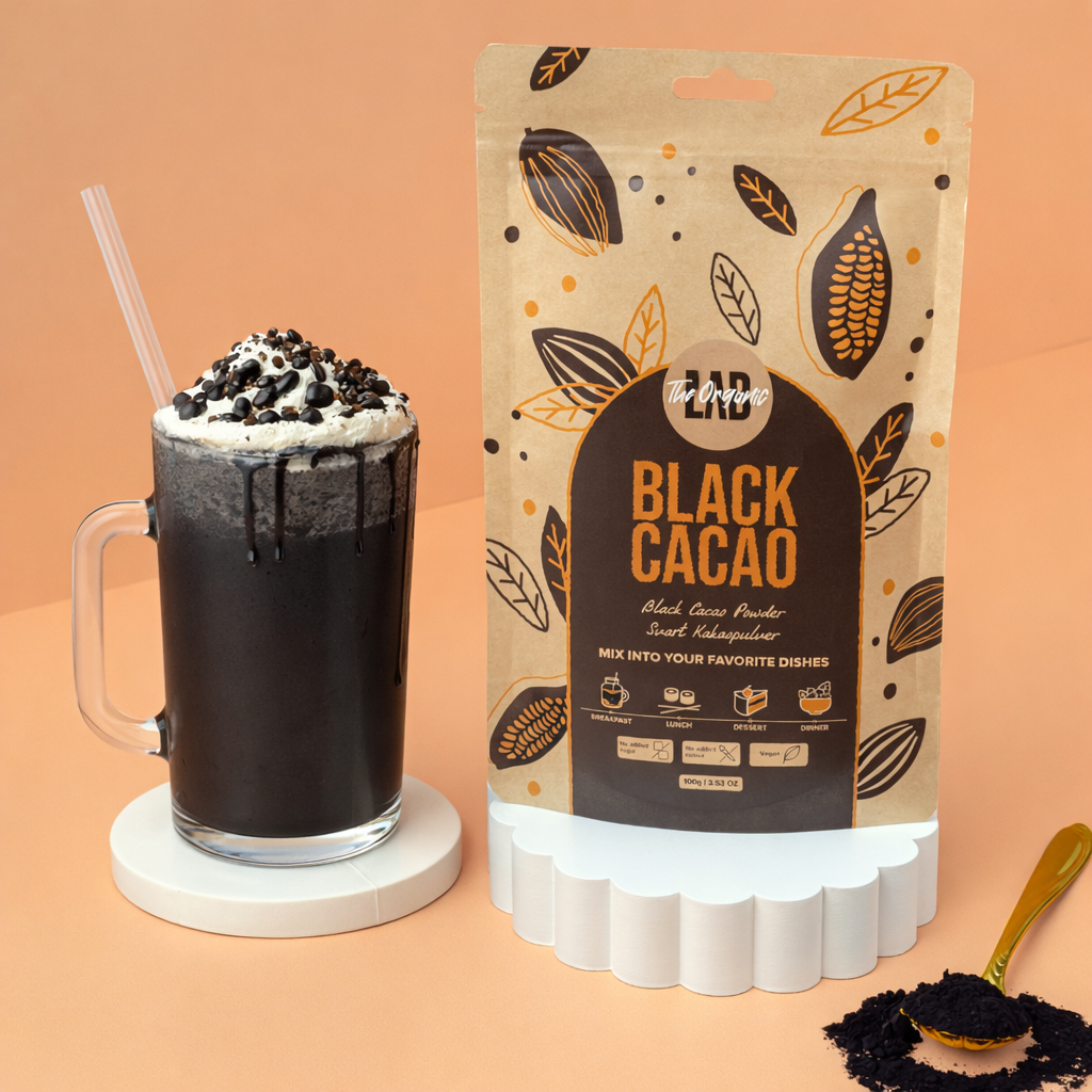 Black cacao iced drink with whipped cream next to a 100 g pouch of The Organic Lab Black Cacao Powder